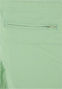 Világoszöld anyagú sort, amely diszkrét zippzáros hátsó zsebbel és elastikus derékrésszel rendelkezik, texturált felülettel és kontrasztos varrással.