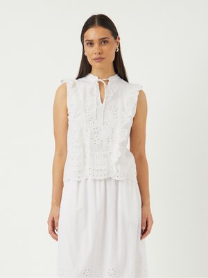 Blouse blanche sans manches avec un col volanté, des détails en œillets et une fermeture à nouer. Tissu doux et broderie détaillée le long de l'ourlet.
