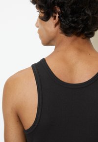Camiseta sin mangas negra de canalé con un diseño clásico de espalda de nadador. Textura suave con costuras reforzadas que mejoran la durabilidad.