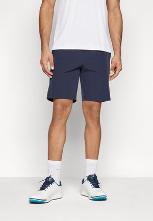 Granatowe szorty mają prosty krój i gładką tkaninę. Zestawione z białymi butami sportowymi i skarpetkami, tworzą swobodny sportowy look.