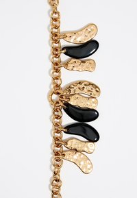 Bracelet en chaîne dorée avec des accents noirs et dorés texturés alternés en forme de gouttes. Présente une finition brillante et des détails de surface complexes.