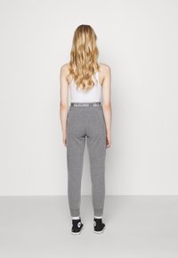 Grå sweatpants med en figursydd design, elastisk midja med vit "Hollister"-logotyp och muddar vid anklarna, parat med svarta sneakers.