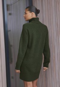 Strickkleid in Olivgrün mit hohem Kragen, gerippten Bündchen und Saum; strukturierter Stoff mit körperbetontem Schnitt.