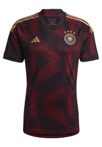Saksan maajoukkueen jalkapallosetti, tummanpunainen, jossa on sahalaitakuviota, mustia yksityiskohtia, v-pääntie, kolme kultaa olevaa raitaa hartioilla ja emblemia rinnassa.
