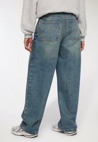 Jeans in denim azzurro chiaro, dal taglio ampio e con una texture lavata, dotati di due tasche posteriori e dettagli di cucitura a contrasto.