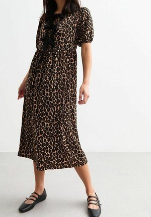 Nainen, jolla on midi-pitkä leopardikuvioinen mekko, jossa on puffihihat ja mustat rusettilisäykset, yhdistettynä mustiin kolmen remmin tasakenkiin.