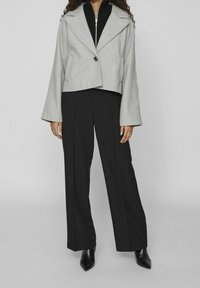 Šedá zkrácená bunda se širokými rukávy, zapínáním na knoflíky a dvěma bočními kapsami, kombinovaná s černými širokými kalhotami a černými špičatými botami.