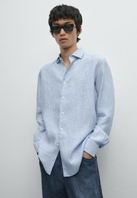 Camicia azzurro chiaro a righe con bottoni, realizzata in tessuto, caratterizzata da una vestibilità comoda, maniche lunghe e una texture morbida, abbinata a jeans di denim scuri.