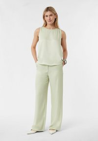 Jasnozielona bluzka bez rękawów połączona z dopasowanymi, szerokimi spodniami. Gładki, miękki materiał o luźnym kroju i minimalistycznym designie.