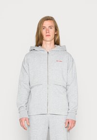 Rozpinana bluza z kapturem w jasnoszarym kolorze, wykonana z bawełny, z kieszenią z przodu, kapturem oraz czerwonym logo "NIGHT ADDICT" na lewej piersi. Gładka tekstura.