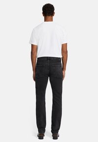 Les jeans en denim noir ont une coupe slim, cinq poches et des passants de ceinture. Le tissu a une finition texturée et un aspect légèrement délavé.