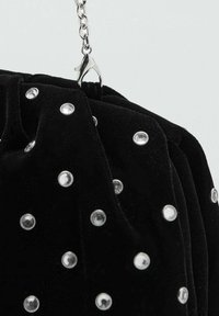 Bolso de mano de terciopelo negro con tachuelas plateadas y una correa de cadena. Presenta un diseño fruncido y un cierre de broche. Superficie texturizada.