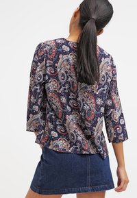 Marinblå blus med paisleymönster och trekvartsärmar, med rika färger och lös passform, ihop med en jeanskjol.