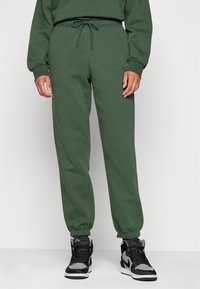 Gröna bomullsträningsbyxor med elastiska ärmslut, dragsko i midjan och sidofickor, i kombination med svarta högklackade sneakers.