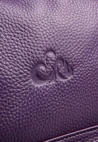 Borsa in pelle viola con superficie texturizzata e dettaglio logo impresso, che mette in risalto una finitura morbida e a pietra.