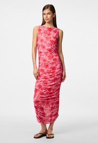 Bez piedurknēm rozā ziedu maxi kleita ar sakopotu tekstūru. Iezīmēta ar laivu formas kakla izgriezumu un sānu rušingu, kopā ar melnām plakanām sandalēm.