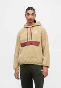 Khaki fleecová mikina s marhuľovým saténovým panelom na hrudi, predná vrecková kapsa a kapucňa so šnúrkou; obsahuje biele logo Nike.