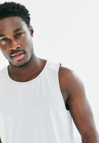 Weißes sportliches Tanktop mit strukturiertem Design, enganliegendem Schnitt und weiten Armlöchern. Verfügt über minimale Akzentnähte an den Schultern.