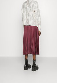 Blusa bianca con motivo floreale e maniche lunghe, abbinata a una gonna midi plissettata bordeaux. Stivali alla caviglia neri con tacco chunky completano l'outfit.