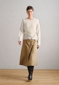 Krēmkrāsas džemperis ar vaļīgām piedurknēm, kopā ar bēšu svārkiem. Apģērbam ir plaša, teksturēta josta ar sprādzīti un brūnas, līdz ceļiem sniedzošas zābaki.