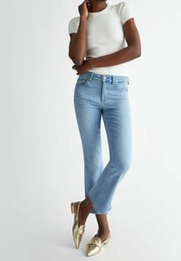 Jasnoniebieskie dżinsy z rozszerzanym dołem, zestawione z błyszczącymi złotymi butami na obcasie z odkrytymi piętami i spiczastym noskiem. Górna część to prążkowana biała koszulka z krótkim rękawem.