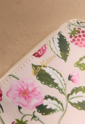 Zbliżenie narożnika materiału w kwiatowy wzór, z zielonymi liśćmi, różowymi kwiatami i złotym logo „Cath Kidston” na beżowym tle.