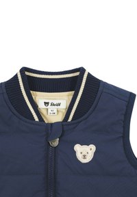 Gilet senza maniche blu navy con colletto a coste, rifiniture a strisce crema e un piccolo ricamo di un orsetto sul petto. Chiusura a zip e tessuto morbido.