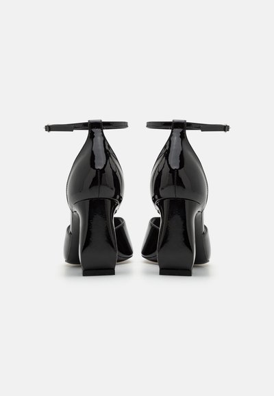 Black patent leather heels with ankle strap, squared toe, and chunky heel design. Glossy texture, sleek silhouette, minimal accents.