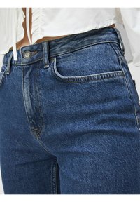 Jeans in denim blu scuro con un classico design a cinque tasche, dotati di chiusura con bottone e cuciture a contrasto lungo le cuciture.