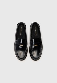 Μαύρες δερμάτινες loafers με λεία φινίρισμα, διακοσμητική ραφή και μικρή μεταλλική λεπτομέρεια στο μπροστινό μέρος. Διακριτό λογότυπο στην εσωτερική σόλα.