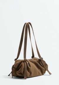 Brown soft fabric shoulder bag with long adjustable straps and zipper closure, displayed against a plain light background.