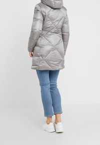 Zilveren opblaasjas met een capuchon, met een doorgestikt ontwerp en elastische manchetten. Gecombineerd met lichtblauwe jeans en witte sneakers.