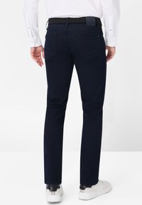 Pantalones azul marino de corte slim, fabricados en una mezcla de algodón, con bolsillos traseros y un cinturón negro texturizado. Combinados con zapatillas blancas.