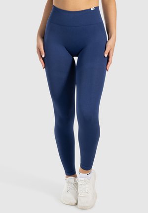 Navyblauwe leggings van rekbare stof met een hoge tailleband. Glad textuur en taps toelopende pasvorm, gecombineerd met witte sportschoenen.