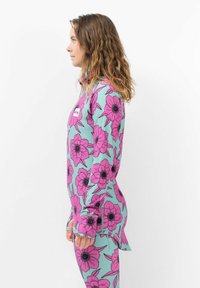 Ensemble de rash guard floral avec un fond vert menthe et de grandes fleurs roses avec des centres noirs, fabriqué en tissu léger et extensible.