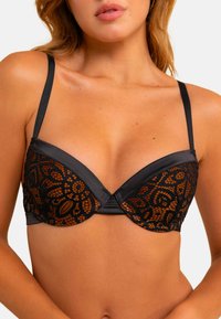 Soutien-gorge noir au design structuré avec des détails en dentelle dans un motif complexe, en matière satinée et avec des bretelles réglables.