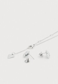 Σετ ασημένιων κοσμημάτων που περιλαμβάνει δύο ζευγάρια σκουλαρίκια: ένα στρογγυλό καρφωτό και ένα με καμπυλωτό σχέδιο, μαζί με μια λεπτή αλυσίδα. Περιλαμβάνει και ένα γούρι.