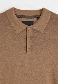 Brązowa koszulka polo z teksturowaną tkaniną, złożonym kołnierzykiem i plisą na trzy guziki. Czarno-biały paskowany akcent wewnątrz kołnierzyka.