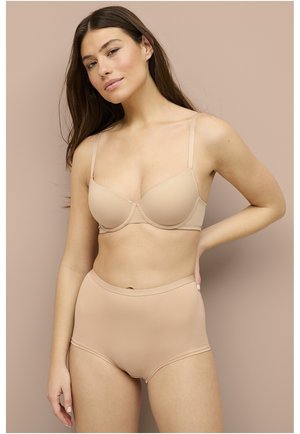 Nude draadloze beha met gladde cups en verstelbare banden, gecombineerd met hoge nude slipjes. Zachte, naadloze stof voor comfort.