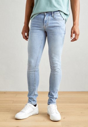 Vaqueros skinny azul claro fabricados con una mezcla de algodón, con una cintura regular, diseño de cinco bolsillos y detalles de costura, combinados con zapatillas blancas.