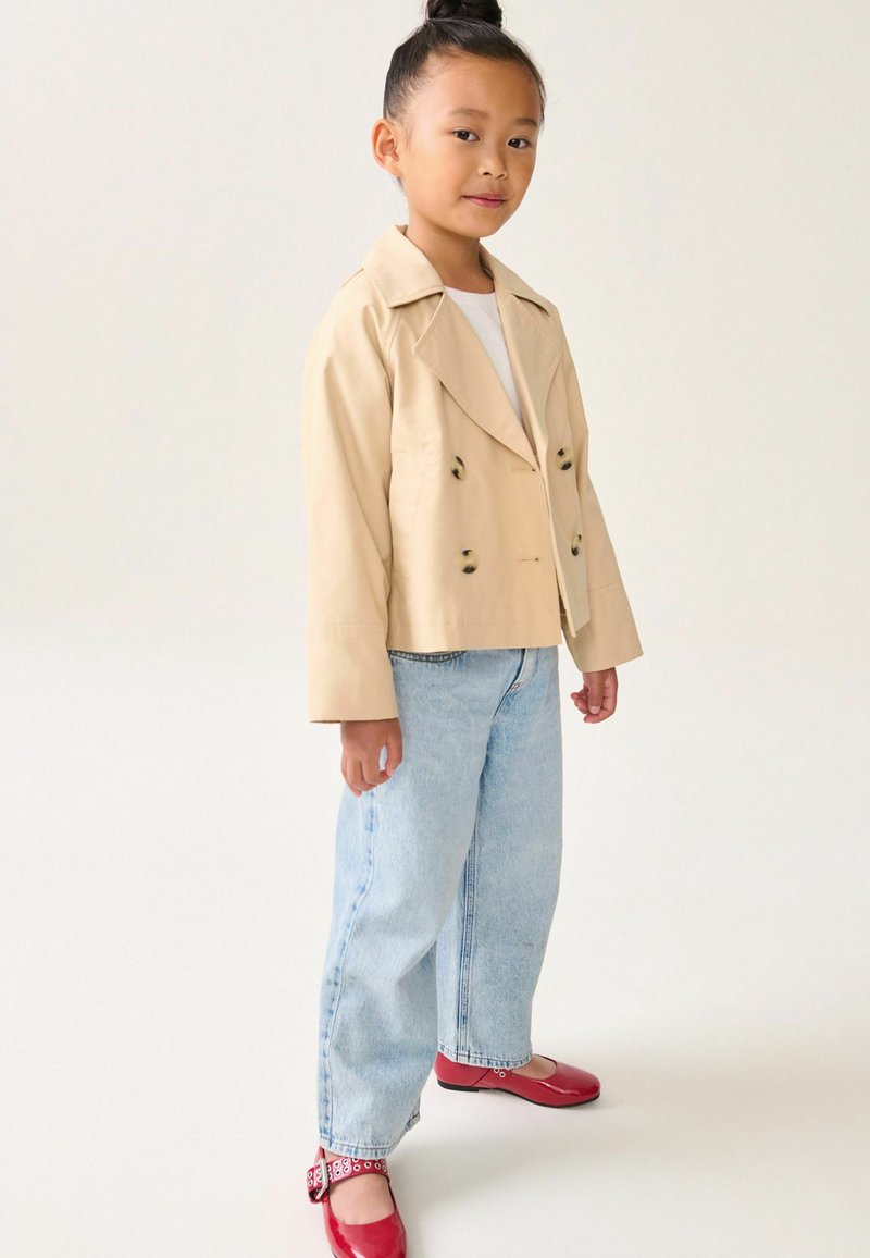 Beige cropped dubbelzijdige jasje, lichtblauwe rechte jeans en rode ballerina's met strikaccent. Lege textuur, op maat gemaakte ontwerp.