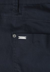 Tissu bleu marine foncé en gros plan montrant une petite poche avant avec rivet en métal et une étiquette de marque argentée "Street One".