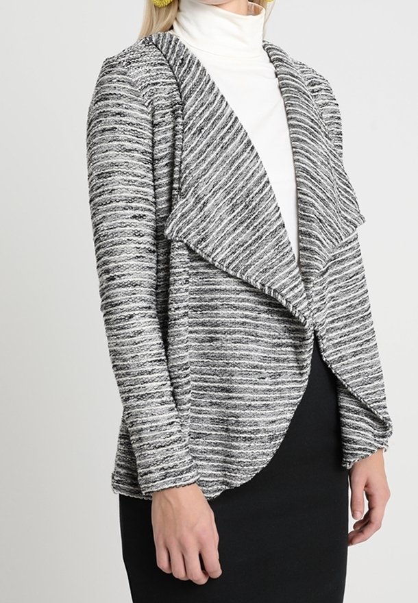 Open-front cardigan made of textured, black-and-white striped knit material; features draped collar and sleek silhouette, paired with a white turtleneck.