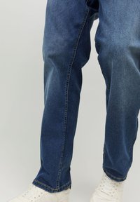 Vaqueros de denim azul oscuro con un corte recto. Presentan costuras visibles y un ligero desgaste. Combinados con zapatillas blancas.