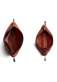 Astucci rettangolari con cerniera in tessuto arancione bruciato, con accenti neri, una texture liscia e fodera interna di colore chiaro.