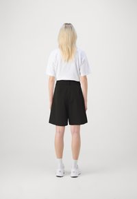 Pantaloni corti neri su misura con una vestibilità comoda, dotati di tasche laterali e una vita a media altezza, abbinati a una maglietta bianca e scarpe da ginnastica bianche.