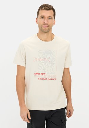 Lys beige t-shirt med korte ærmer, prydet med en grafik i pastelfarvet blå og rød tekst, der angiver "CHASE NEW HORIZONS" og "camel active."
