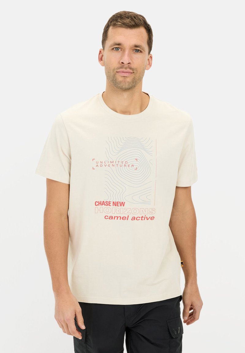 Lys beige t-shirt med korte ærmer, prydet med en grafik i pastelfarvet blå og rød tekst, der angiver "CHASE NEW HORIZONS" og "camel active."