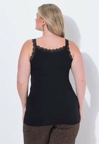 Černý top na ramínka s krajkovým lemováním na ramínkách a výstřihu, vyrobený z hladké látky. Nosit s vzorovanými hnědými kalhotami, které mají uvolněný střih.