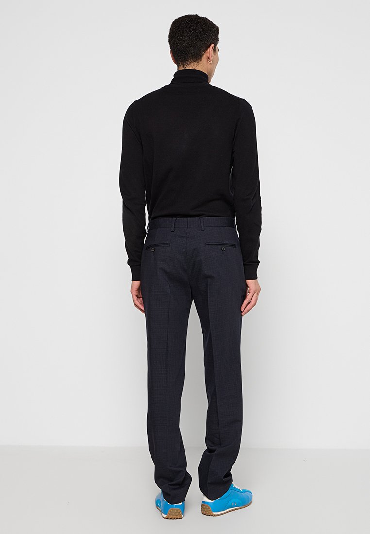 Suéter negro de manga larga y cuello alto, combinado con pantalones oscuros de cuadros grises y zapatillas deportivas azules. Textura suave, ajuste a medida.